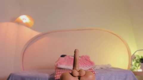 Video of a child's hand holding a toy sword, positioned on a bed with a pink and white checkered blanket, against a soft yellow wall with a glowing lamp.