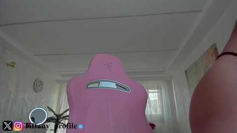 A video of a pink gaming chair with a circular window in the background, set in a bright, modern room.