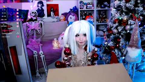 Video of a woman in a white wig, black top, and festive outfit, standing in front of a decorated Christmas tree in a cozy, cluttered room.