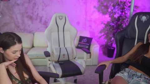 Video of a young woman with long hair in a gaming chair, surrounded by a purple-lit room with a white couch, a plant, and a man in a black hoodie.