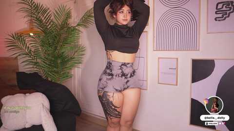 A video of a woman with light brown skin and curly black hair, wearing a black crop top and a high-waisted, patterned skirt, posing in a stylish living room with modern decor and abstract art.