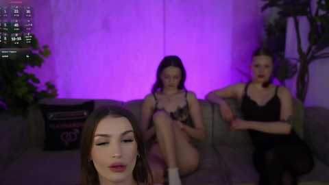 A video shows three women on a gray sofa, bathed in purple light, wearing lingerie, with a fourth woman's face in the foreground.