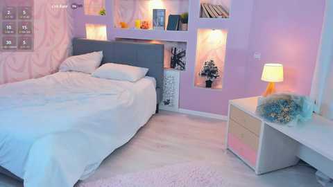 Video of a pastel-themed bedroom with a white bed, gray headboard, light pink walls, built-in shelves, and a cozy white nightstand with a soft lamp.