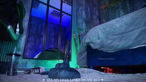 A video of a dimly lit, graffiti-covered bedroom with a blue light, a large bed, and a black dildo on a pedestal, with \"All My Free Licks On My Bio\" text at the bottom.