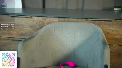 Video of a modern, light blue upholstered chair with a wooden frame against a dark brown wooden wall, with a QR code and a digital screen displaying \"Tap to learn\" in the bottom left corner.