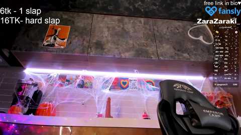 A video of a cluttered, colorful desk with a computer chair, featuring a messy surface with multiple open boxes, a pink dildo, and a Zara bag, lit by a bright white LED strip.