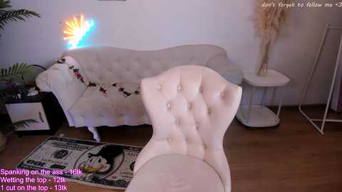 Video of a beige, tufted chair in a modern living room with a neon sunburst light, a potted plant, and a money-themed rug.
