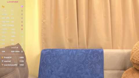 A video of a cozy living room featuring a beige sofa, a blue patterned blanket draped over it, and mustard-yellow curtains. A yellow digital clock with a time of 11:09 hangs on the wall.