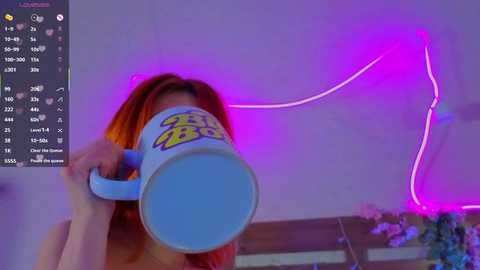 Video of a woman with orange hair holding a blue \"Scooby-Doo\" mug in front of her face. She stands indoors with purple neon lights and a digital display in the background.