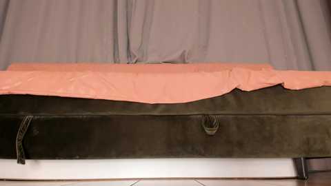 Video of a hospital bed with a grey metal frame and a pink, wrinkled sheet covering the mattress, resting on a white tiled floor.