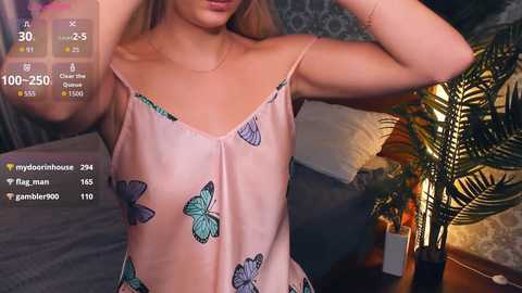 Video of a woman in a light pink, butterfly-patterned camisole, standing indoors with a dimly lit background, displaying live stream metrics.