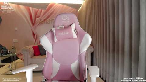 Video of a pink and white gaming chair with the brand \"TCL\" and \"FALCON\" logos, set in a modern living room with beige walls, a couch, and a ceiling fan.