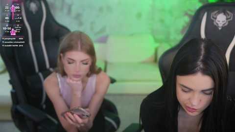 Media: Video of a young woman with straight brown hair, wearing a black jacket, texting on a phone, seated in a gaming chair with a green background.
