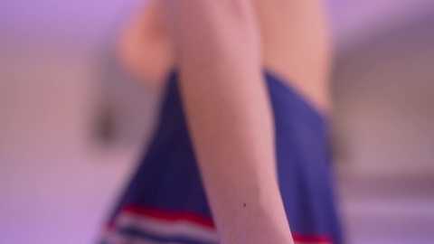 A blurred video of a person's arm and shoulder in a blue dress with red and white stripes, possibly in a bedroom with soft lighting.