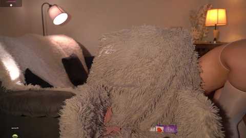 Video of a cozy, dimly lit bedroom with a plush, beige shag rug, a soft, white throw blanket, and a lamp emitting warm light.