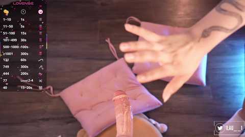 Video of a light-skinned person with tattoos, holding a pink purse and an erect penis. Background shows a dark wooden floor and a digital interface displaying user stats.