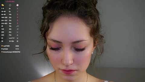 Media: A video of a young woman with fair skin, brown hair in a bun, wearing subtle makeup, with a blurred background.