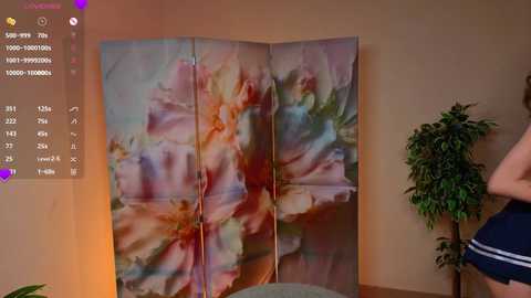 Video of a living room with a large, colorful floral screen, a potted plant, and a person wearing blue shorts, partially visible.