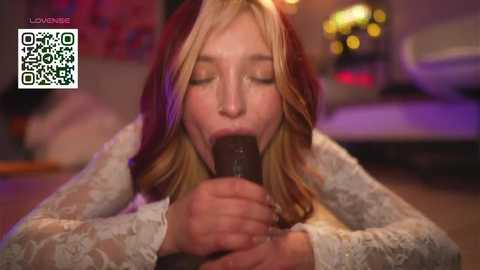 Video of a blonde woman with fair skin, wearing a white lace dress, performing oral sex on a dark-skinned man. Background is blurred with neon lights, suggesting a nightclub setting. QR code in the top left corner.