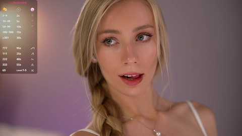 Media: Video of a fair-skinned, blonde-haired woman with a single braid, wearing a white spaghetti strap top, against a blurred purple background.