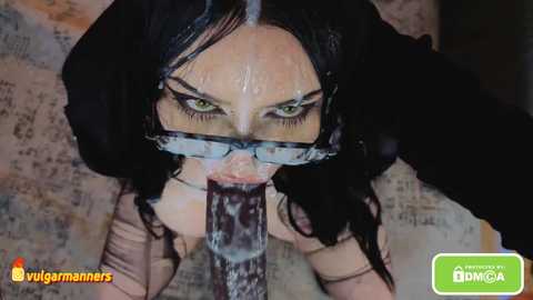 Media: A close-up video of a woman with black hair, wearing glasses and a white blindfold, licking a large, erect penis. Background shows a cluttered room with a map on the wall.