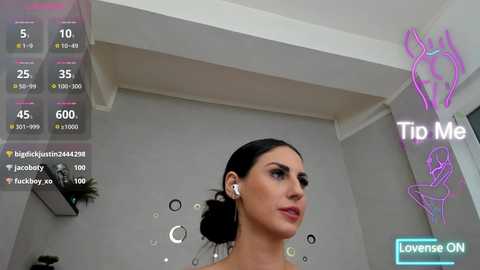 A video of a woman with dark hair in a bun, wearing headphones, in a modern, minimalist room with a white ceiling and gray walls. The image includes virtual health statistics overlayed.