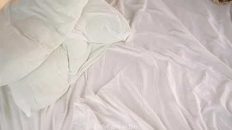 Video of a neatly made bed with a white comforter, pillows, and sheets, showcasing a minimalist, clean aesthetic. The image focuses on the bed's smooth, wrinkle-free surface, indicating meticulous care.