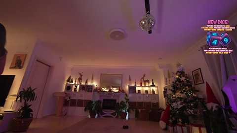Video of a cozy, dimly lit living room decorated for Christmas with a lit tree, a fireplace adorned with candles, and a large, shiny disco ball hanging from the ceiling.