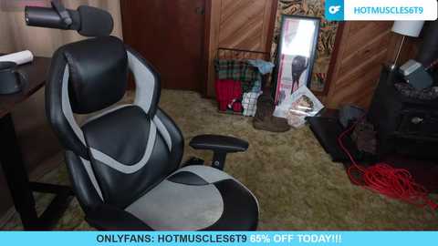 Video of a black and grey gaming chair in a cluttered, carpeted room with a wooden backdrop, a mirror, and a mess of cables and equipment.