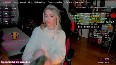 Video of a blonde woman in a cozy living room, wearing a white sweater, surrounded by various digital displays and text messages, indicating an online gaming or streaming context.