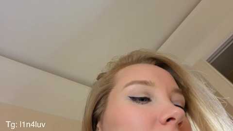 Media: Video of a blonde woman with light skin, wearing makeup with black eyeliner and eyeshadow, captured from a low angle, showing her eyes and nose.