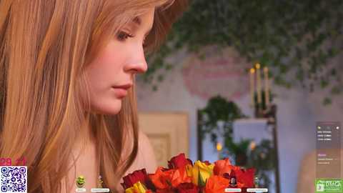 A video of a young Caucasian woman with fair skin and long, straight blonde hair, wearing a light-colored top, holding a bouquet of red and yellow roses. The background features a blurred, softly lit room with a decorative candle holder.