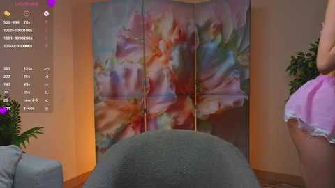 Video of a woman in a pink dress standing beside a floral-patterned room divider, with a green armchair in the foreground.