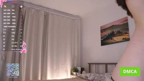 A video of a dimly lit bedroom with a woman partially visible in the foreground, wearing a pink top. The room features a wooden bed, beige curtains, and a landscape painting on the wall.