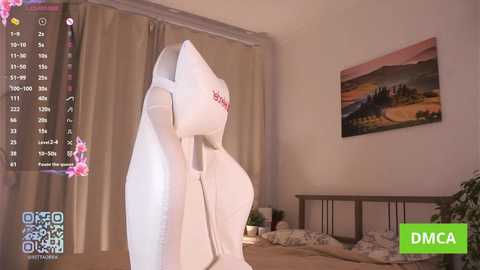 A video of a plush white kangaroo toy with a red tag on its back, positioned on a bed with beige sheets. The background features a window with beige curtains and a landscape painting.