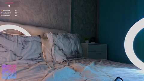 Video of a modern bedroom with a teal wall, white marble-patterned bedding, two round night lights, and a white nightstand.