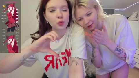 Media: Video: Two young women in casual clothes, kissing each other passionately in a bedroom. Left: fair-skinned redhead with red t-shirt, tattoos. Right: fair-skinned blonde with white t-shirt, tattoos.