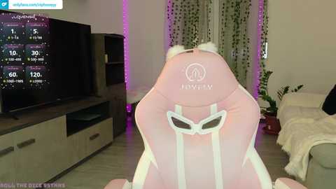 A video of a pink \"Logitech\" gaming chair with cat ears, in a cozy, dimly lit living room with a TV, shelves, and curtains.