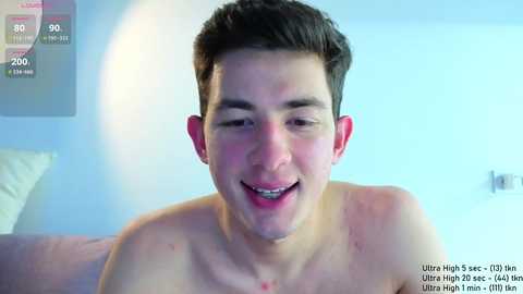 Video of a young, smiling, shirtless man with short dark hair, taken indoors. The background is minimalistic with a white wall and a framed picture. The image includes a fitness app overlay.