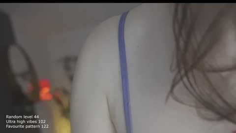 Video of a woman's bare back in a purple bra, taken from a low angle, showing her shoulder and part of her hair. The background is blurred, with text overlay.