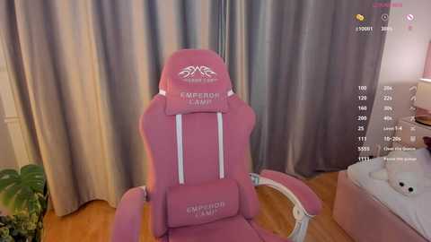 Video of a pink gaming chair with \"Empire MP\" logo, positioned in a cozy, dimly lit room with beige curtains, wooden floor, and a plush toy on the right.