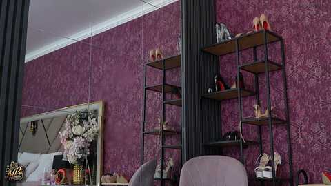Video of a stylish, modern bedroom with deep purple damask wallpaper, black metal shelves holding shoes and accessories, and a mirrored wall reflecting a floral arrangement and bed with a plush, light gray duvet.