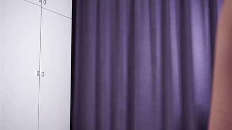 Video of a white wall with a door on the left and a deep purple curtain covering the right side, creating a stark contrast between light and dark.