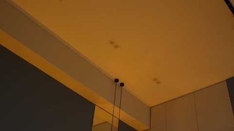 Video of a modern, dimly lit room with a beige ceiling featuring recessed lighting and a black lamp stand. The walls are painted in dark gray. The ambiance is warm and subdued.