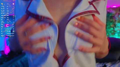 Video of a woman's hands squeezing her breasts through a white, open-collared top, revealing cleavage. Background shows colorful computer screen with various icons and notifications.