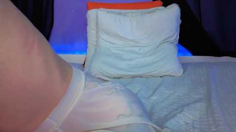 Video of a person lying on a bed, wearing white underwear, with a blue blanket and a white pillow with orange trim in the background.