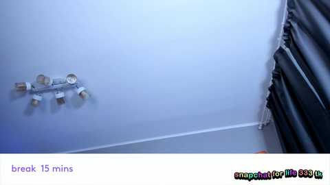 Video of a ceiling-mounted white light fixture with five bulbs in a modern room, featuring a white wall and a dark gray curtain.