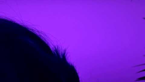 A video of a dark, silhouetted figure against a vivid purple sky, with the subject's hair slightly visible and the background filled with deep purple hues.