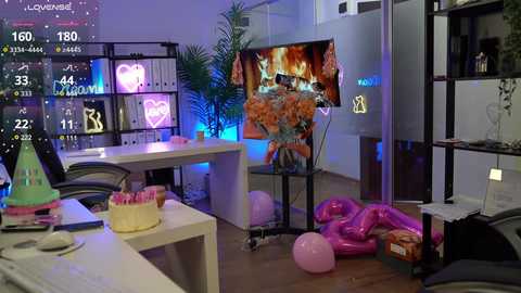 Video of a modern, colorful office room with a large TV screen displaying an animated scene, pink balloons, and a birthday cake on a white desk, vibrant neon lights, and a potted plant.