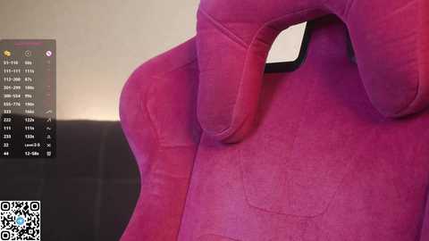 A video of a plush, magenta gaming chair with a large, curved headrest and armrests, set against a plain beige wall. The chair is ergonomic and designed for comfort.
